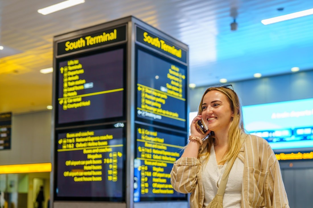 A passenger on the phone beside an airport South Terminal departures board